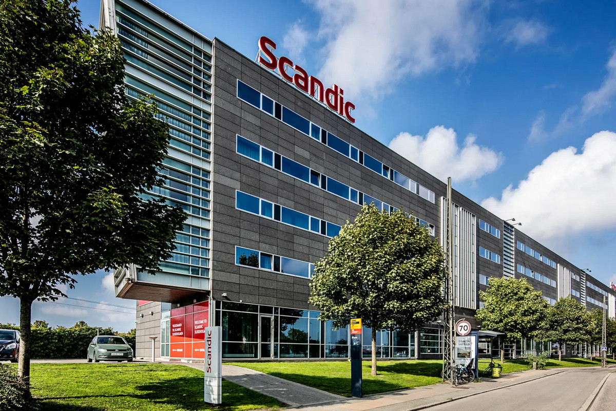 Large hotel building with the Scandic logo on top and green trees in front
