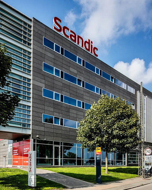 Large hotel building with the Scandic logo on top and green trees in front